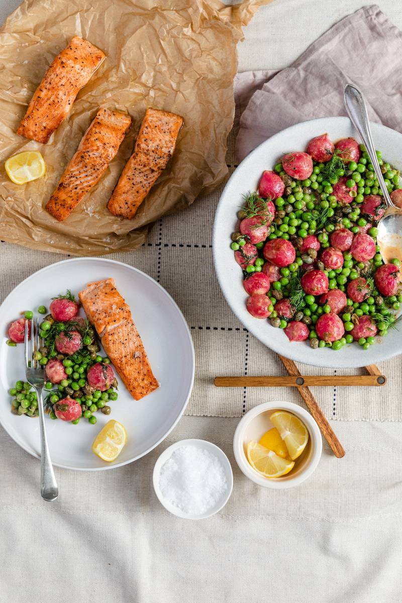 trout, radishes and peas laid out on a table with a half of lemon to sprinkle