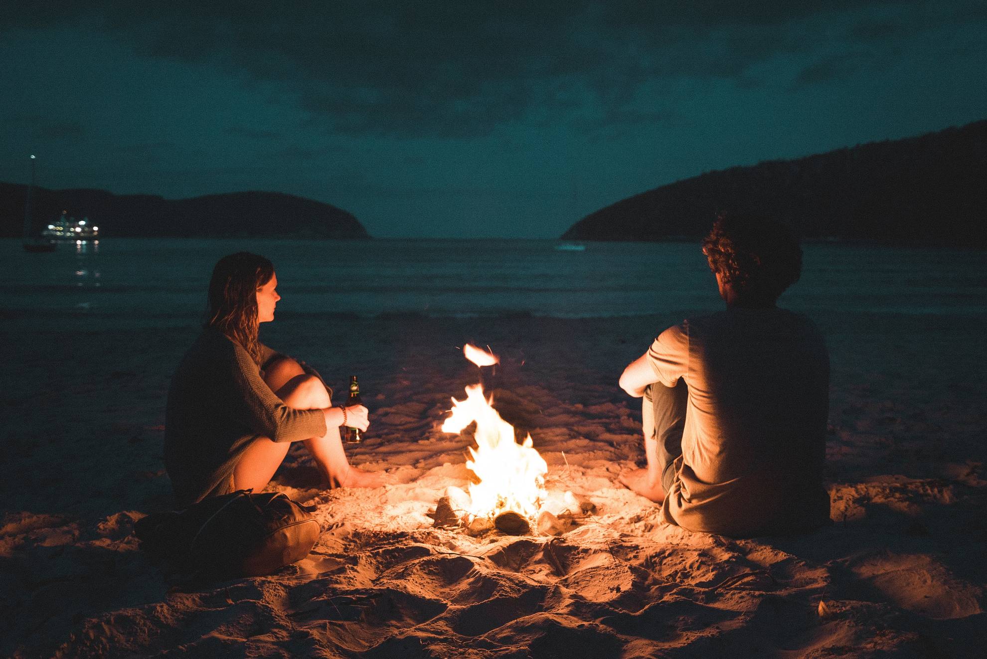 a couple sit by an open fire on the beach