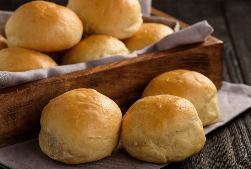 Lot of freshly baked bread rolls on wooden tray