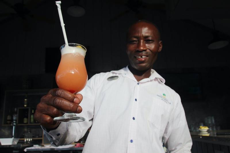 Bartender Kevin Isaacs holds up a cocktail glass containing a frothy peach pink drink and straw