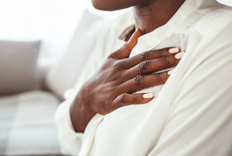 Woman in white top puts hand on chest when struggling to breathe