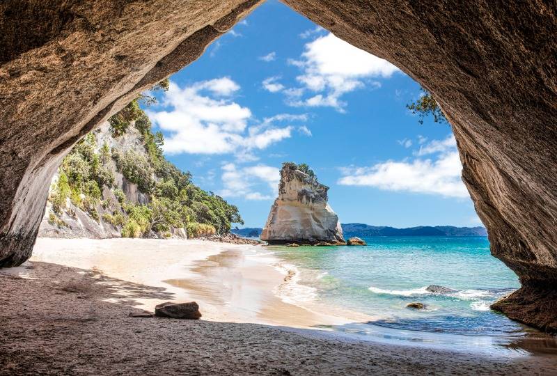 View of beach and crystal blue sea through stone archway of Cathedral Cove, Coromandel in New Zealand
