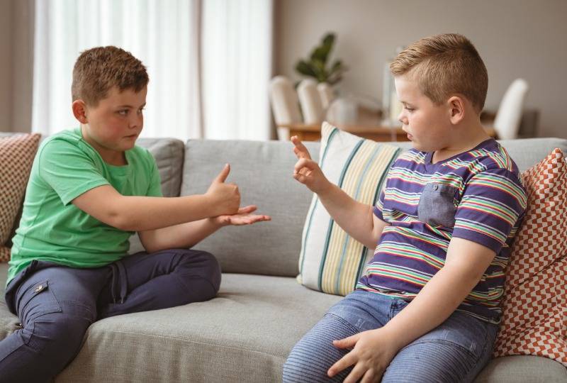 Two boys sit on a sofa and use sign language to speak