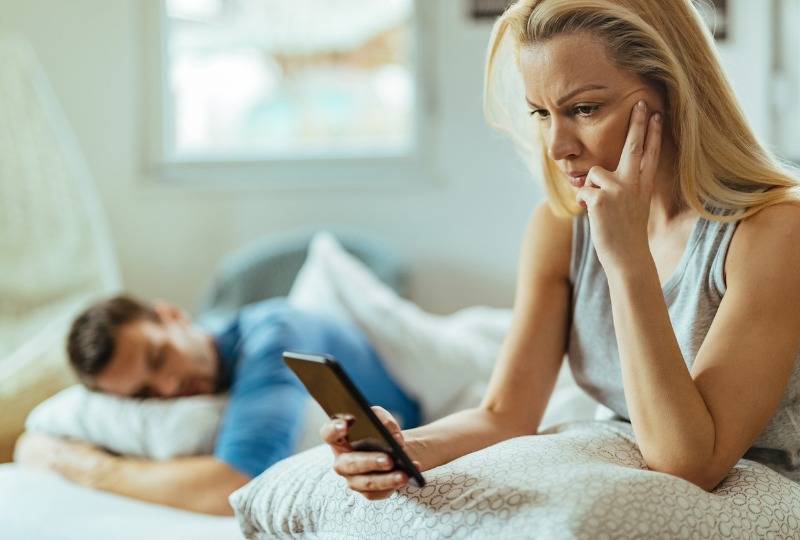 Woman checks cheating partner's phone while sat in bed