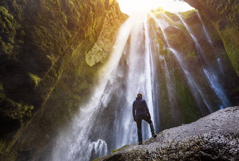 Hiker stands in front of Gljúfrabúi waterfall in Iceland