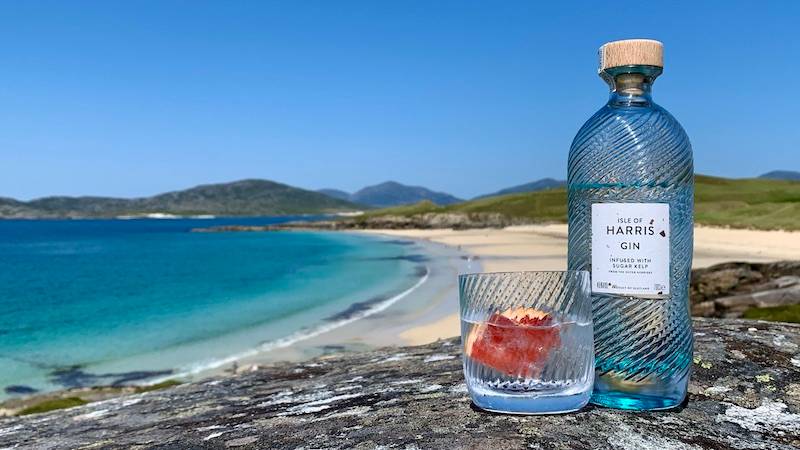 Glass bottle of Harris gin with beach and blue sky in background