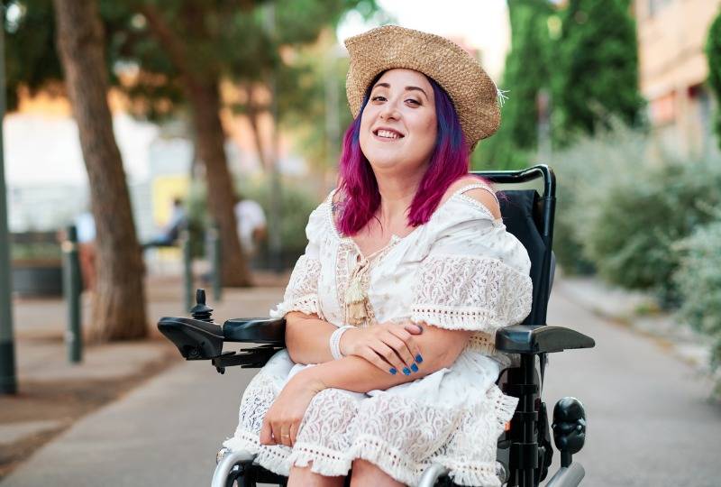 Woman with pink hair sits in wheelchair in street