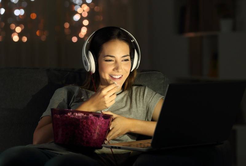 Woman watching film on laptop with headphones and bowl of popcorn