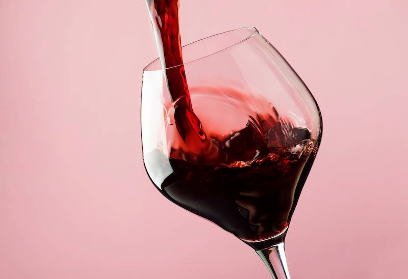 Red wine being poured into glass against pink background