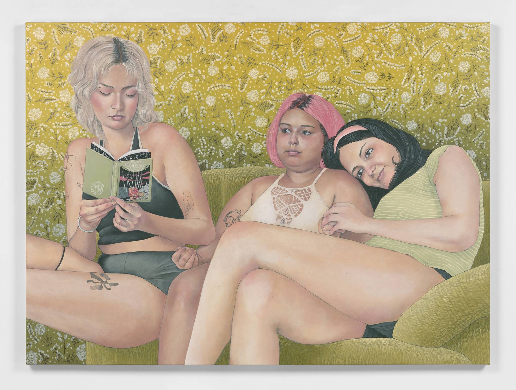 three girl friends recline on a sofa, heads leaning on each others shoulders