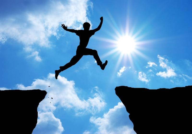 Person jumping between cliffs under blazing sun and blue sky