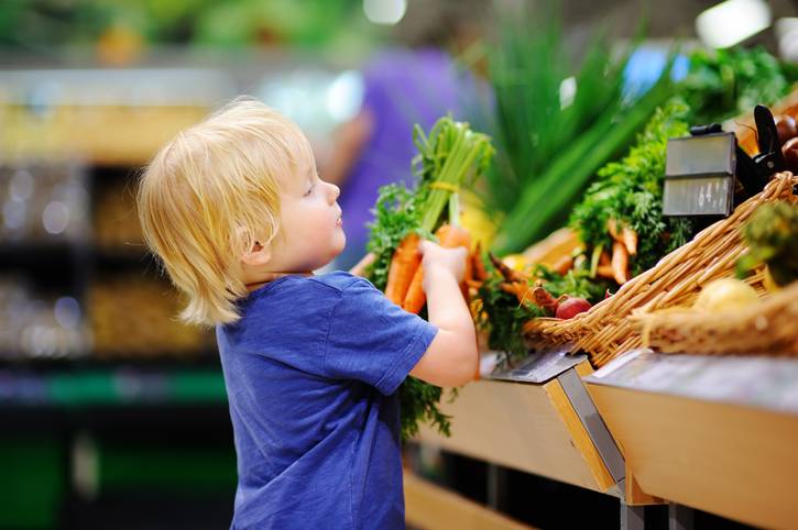 a child getting involved in grocery shopping, holding carrots