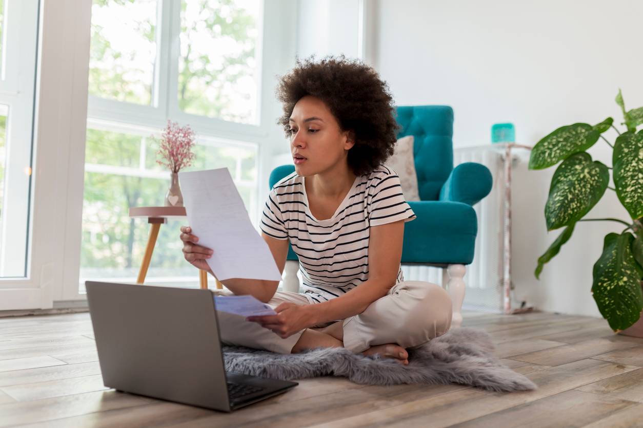 Woman in the middle of a living room studying a piece of paper in front of her laptop