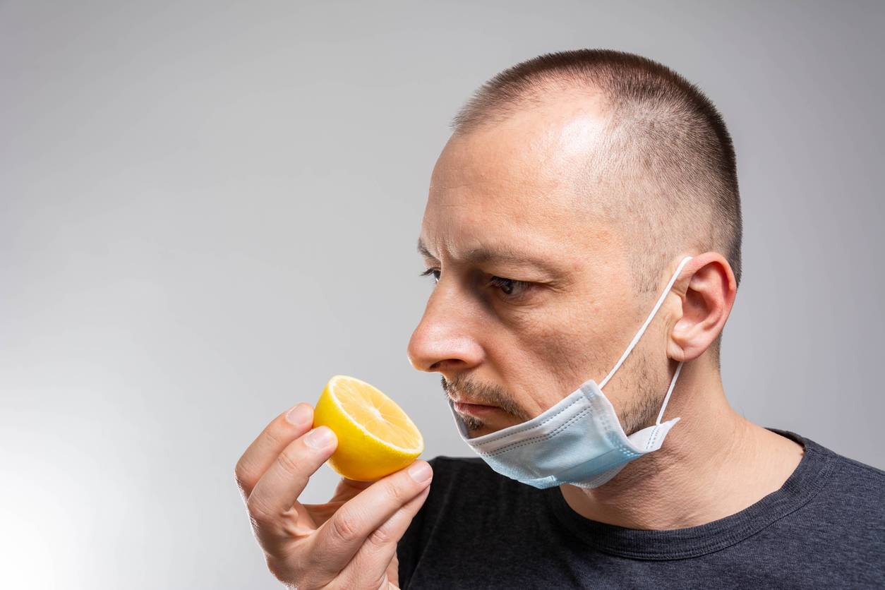 Man with surgical mask around neck trying to smell a lemon