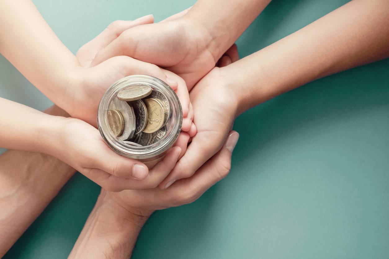 Child and parent hands holding money jar