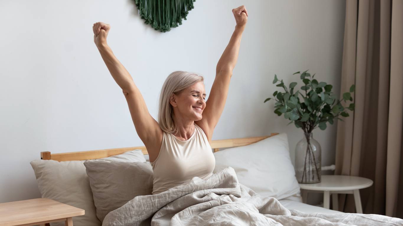 An older white woman stretching in bed