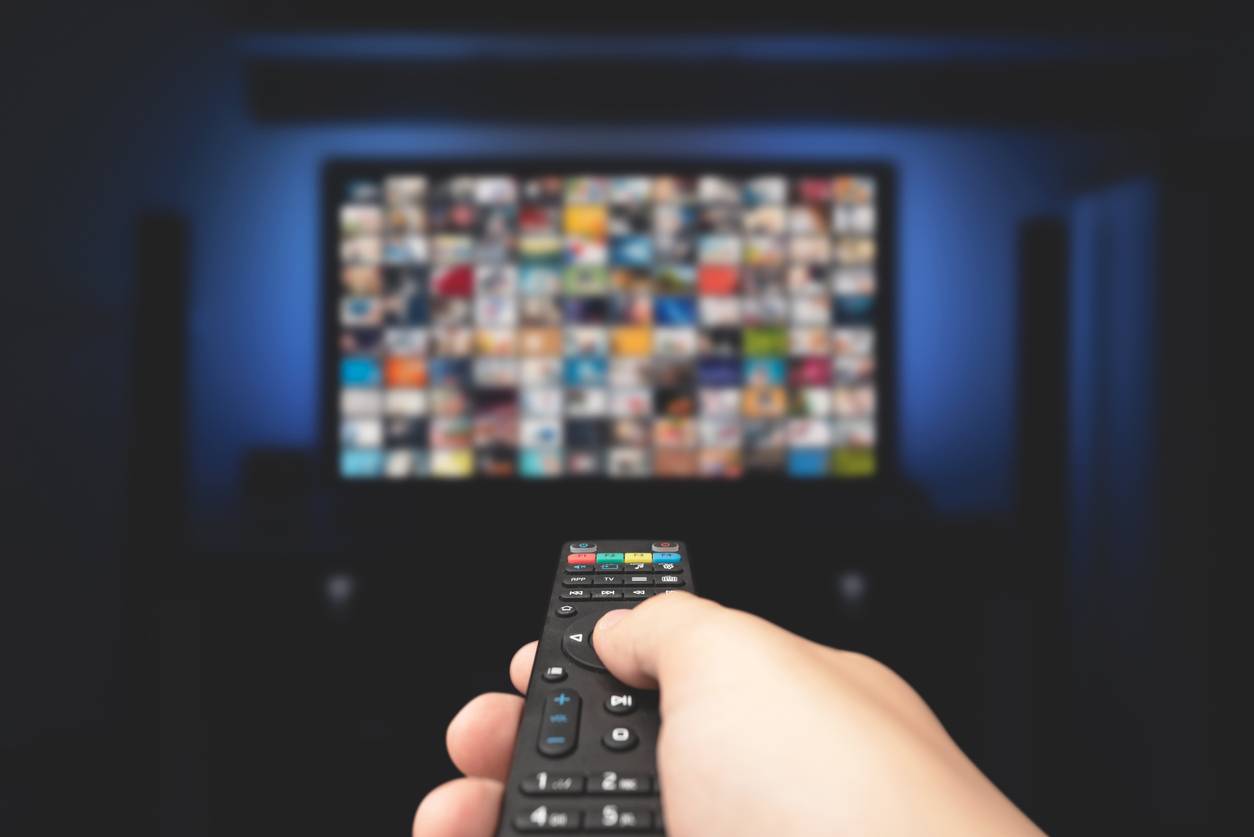 Someone's hand pointing a TV remote at a screen