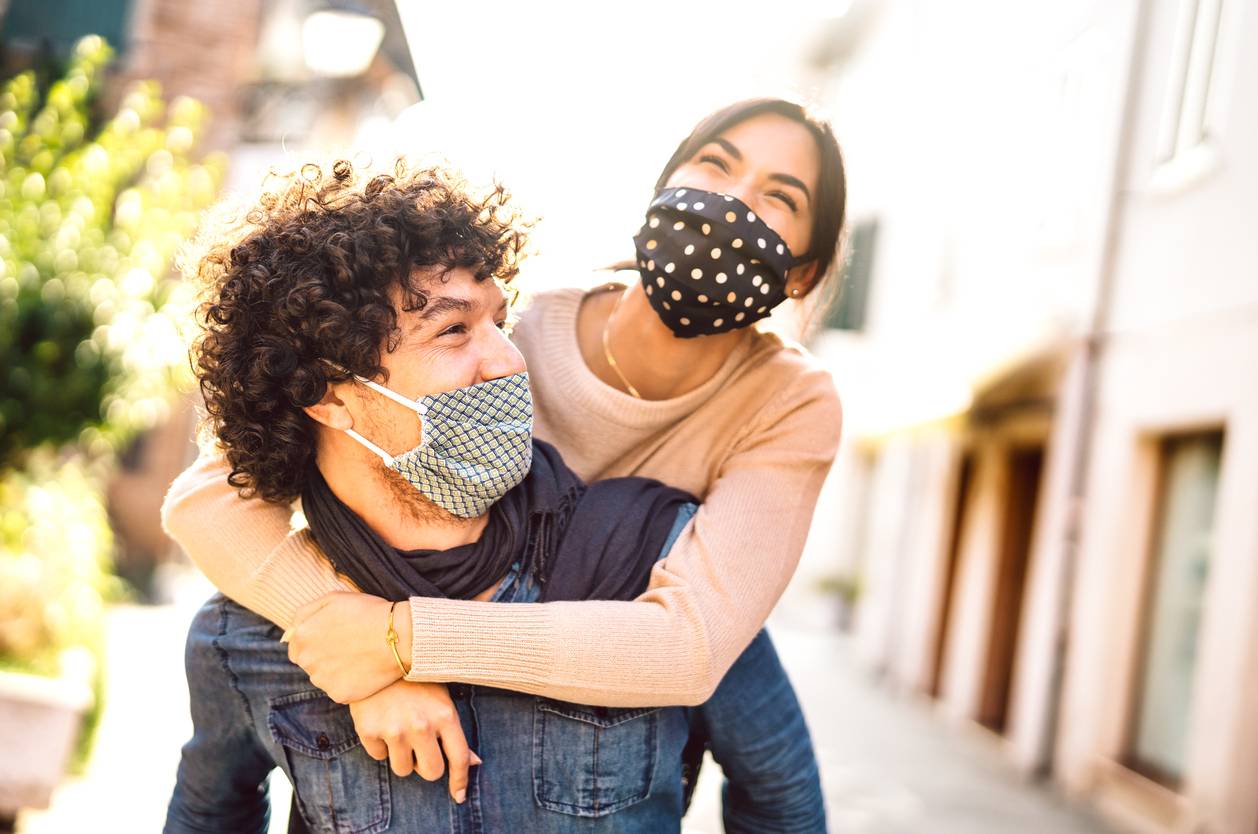 A happy couple having a piggyback while wearing masks