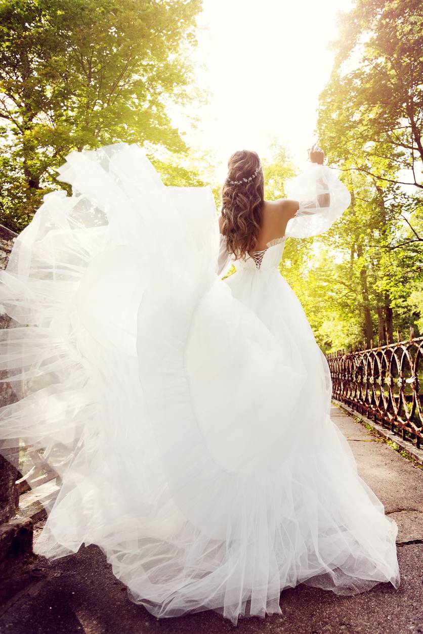 Rear view of Happy white Woman in Elegant Wedding Dress walking in Summer Park