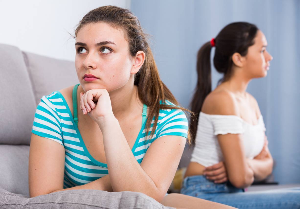 Two women angry with each other and sat on a sofa but facing away from each other